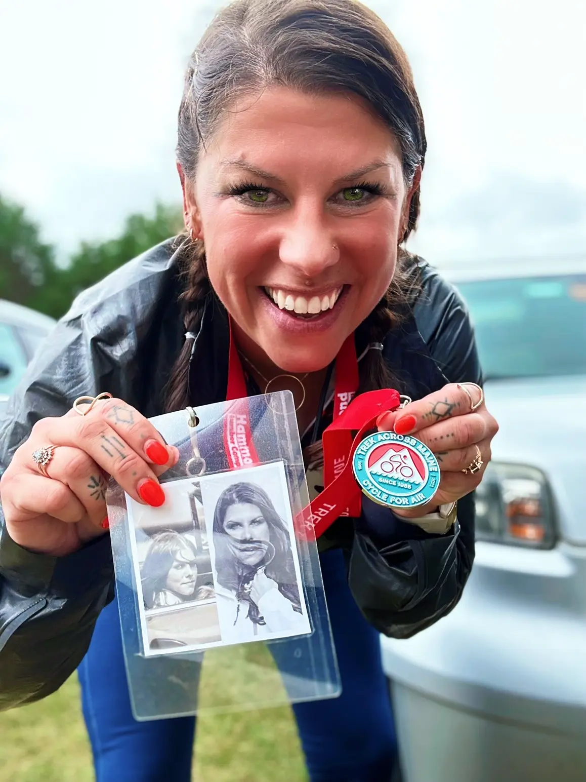 Lizzie smiling as she holds up a Trek Across Maine medal and a badge with vintage photos.