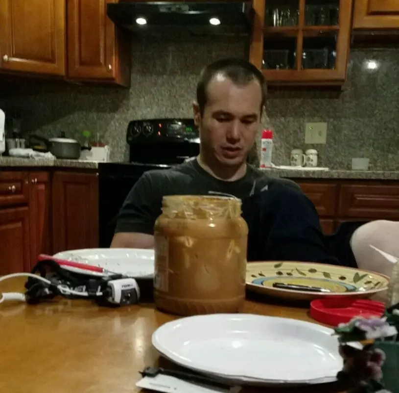 Michael sitting at a kitchen table behind a big jar of peanut butter.