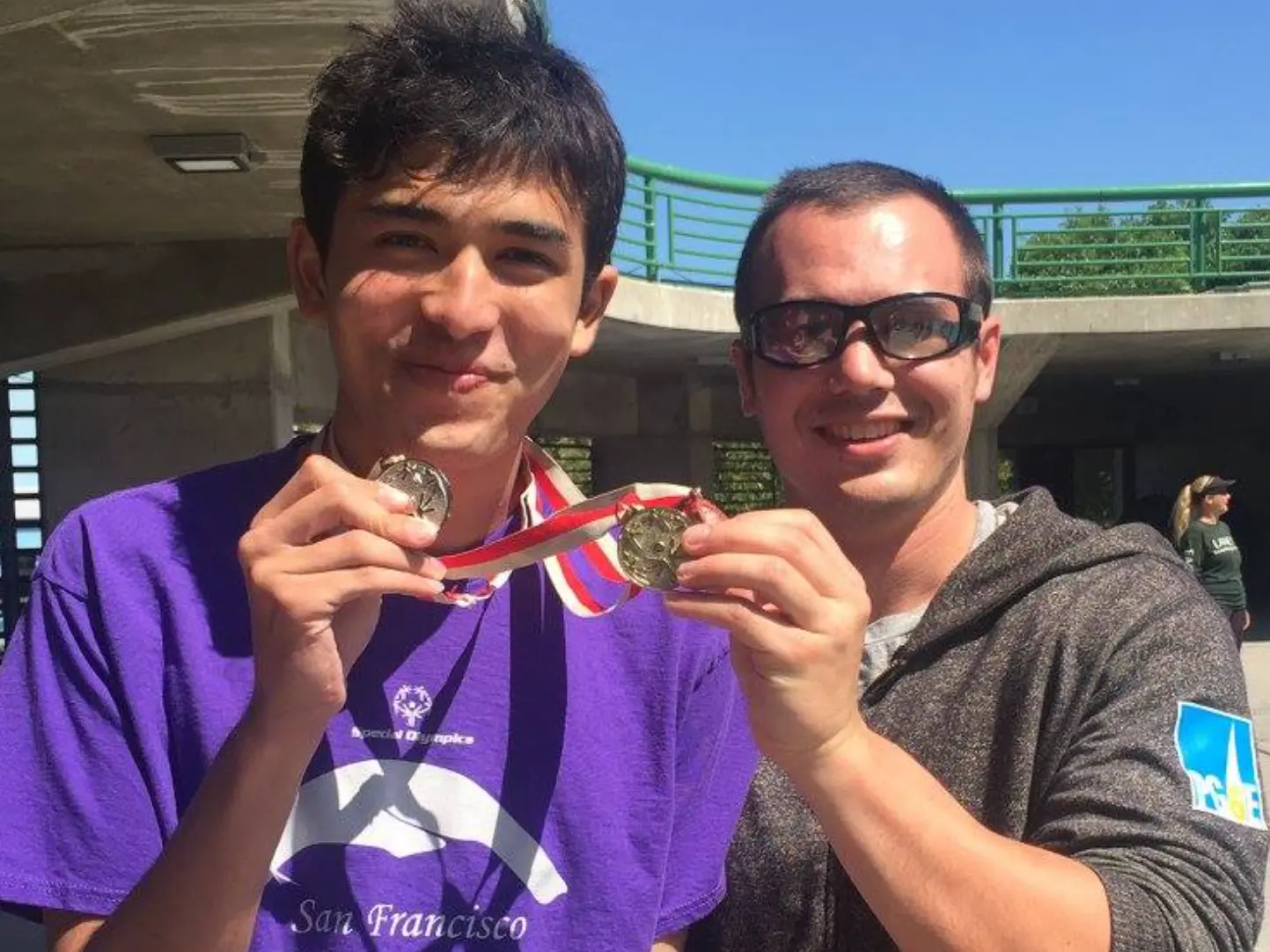 Two young men smiling as they hold up a medal together.