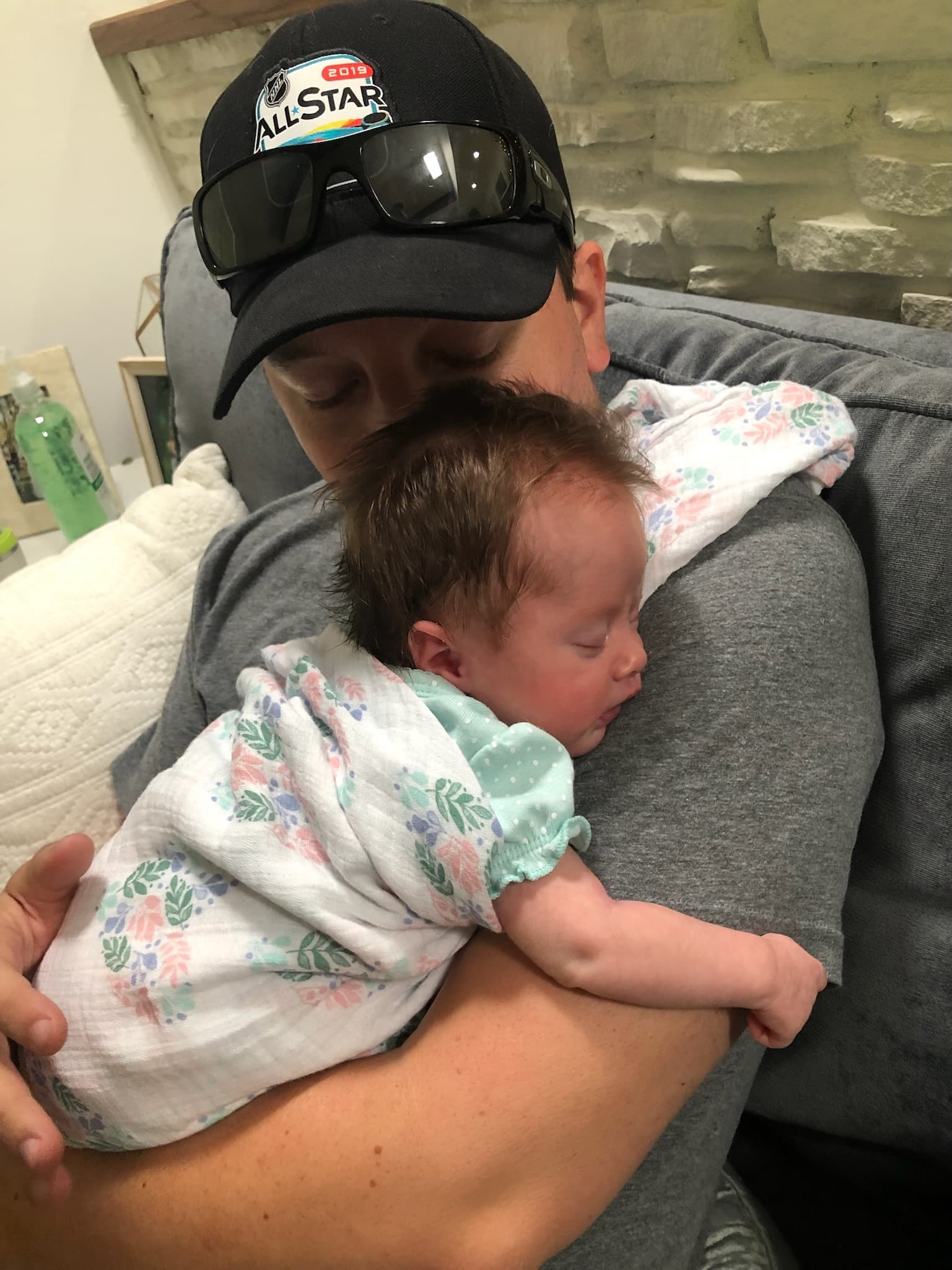 Man in a baseball cap cradling a sleeping newborn against his shoulder