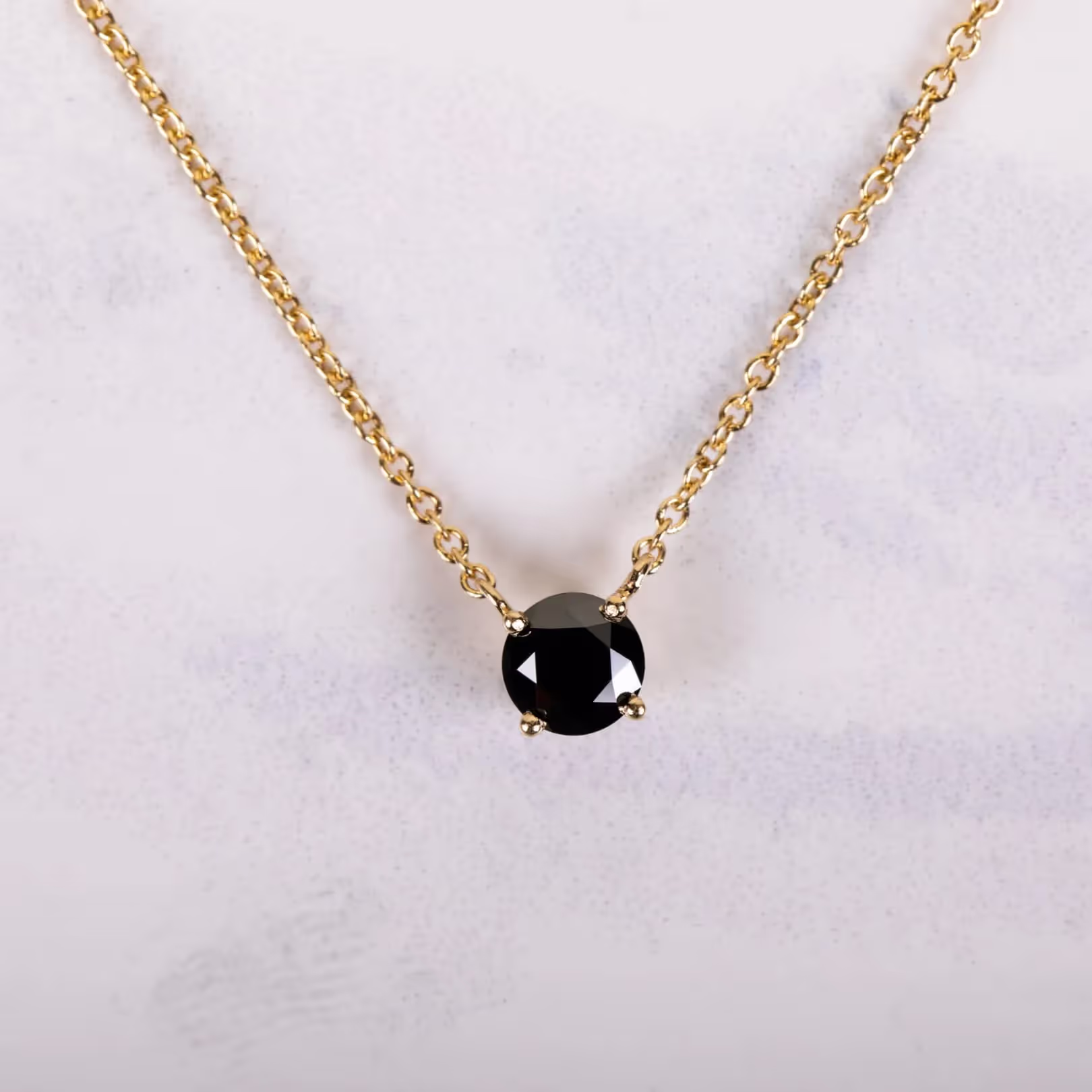 Gold chain necklace with a single round black gemstone pendant.