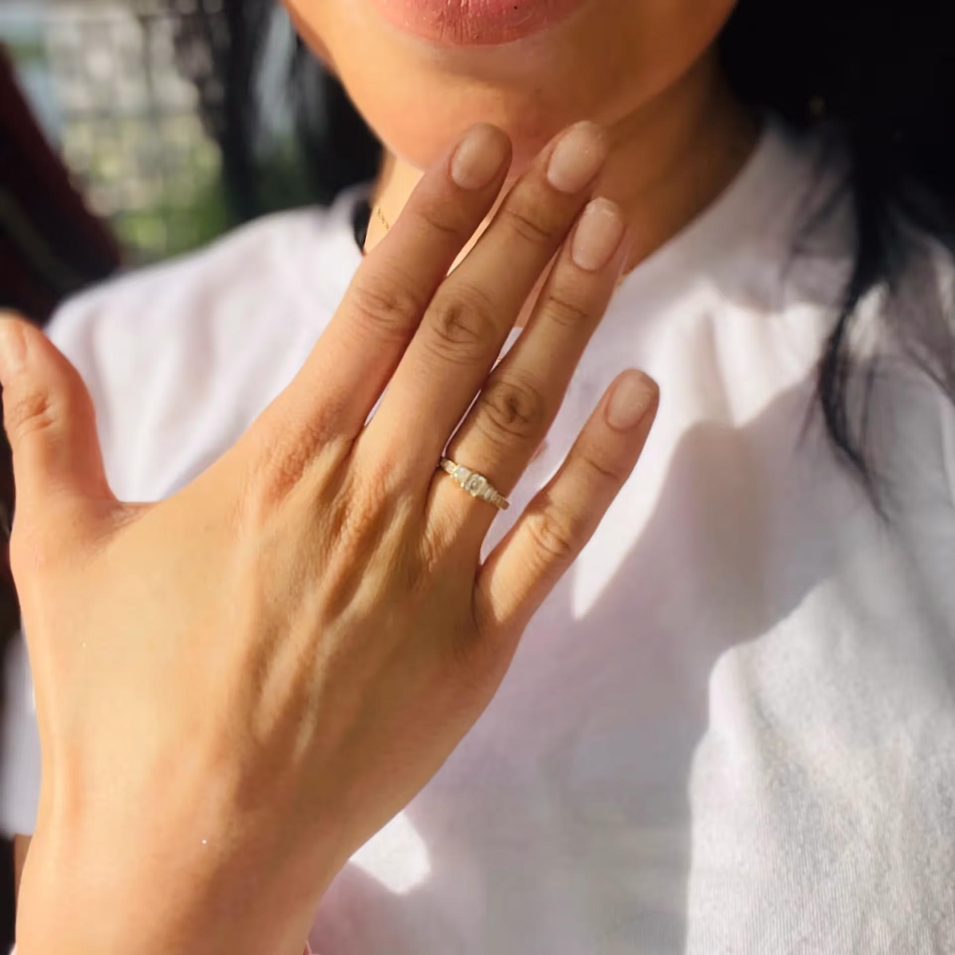 Close-up of a hand with a diamond ring on the ring finger, against a person wearing a white shirt.