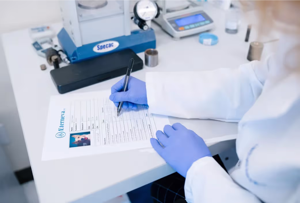A technician in a white lab coat and blue gloves filling in a pet record beside a photograph of a dog.