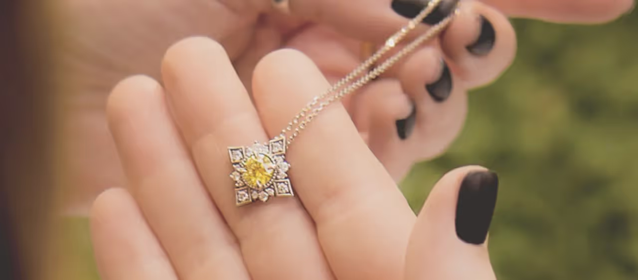 A hand holding a necklace with a yellow gemstone pendant surrounded by smaller clear stones.