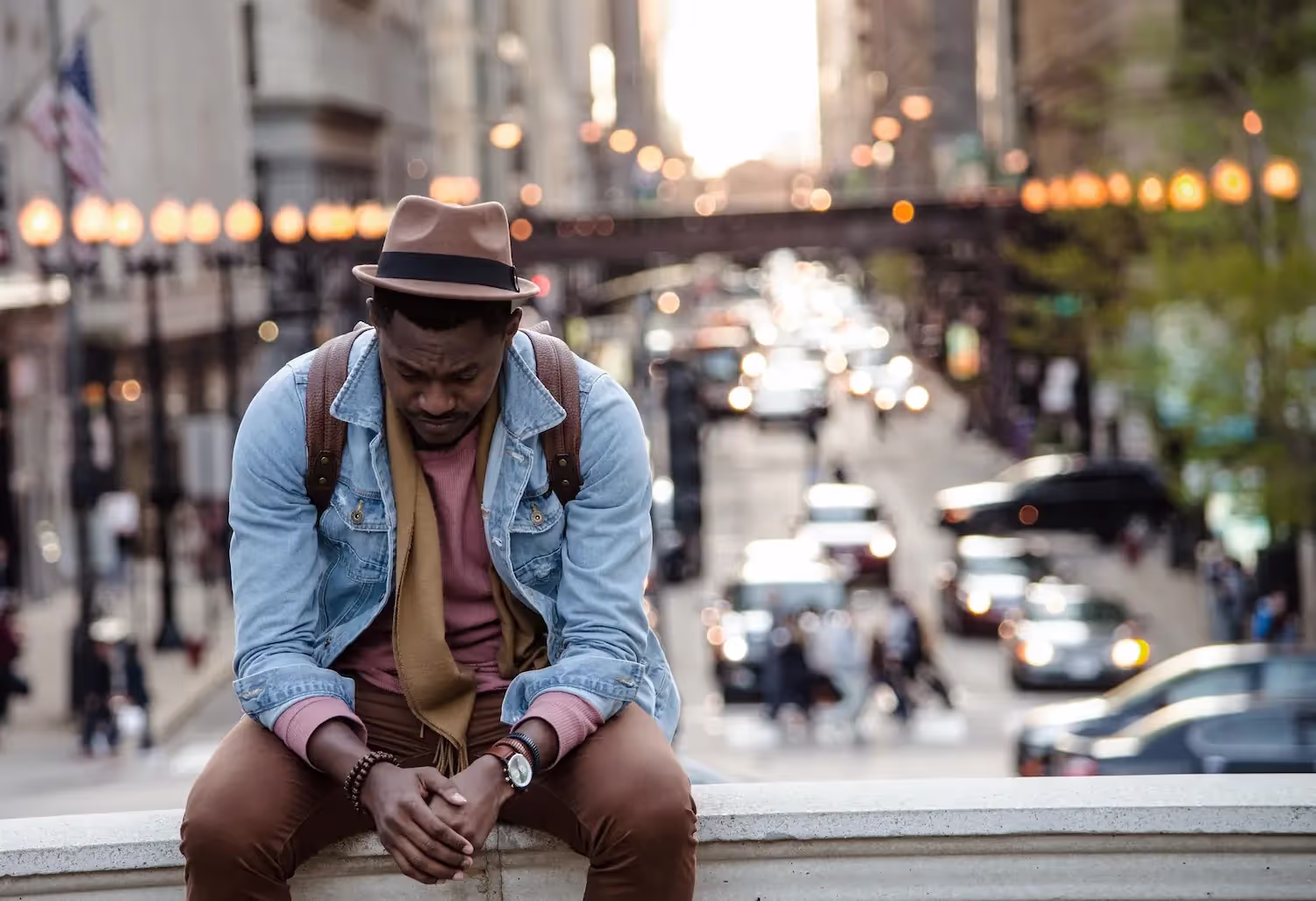 Man in a hat and denim jacket sitting on a wall.