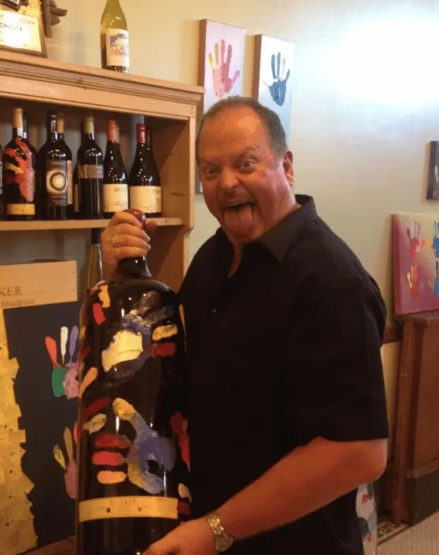 Rudy grins and sticks out his tongue while holding an oversized hand-painted wine bottle.