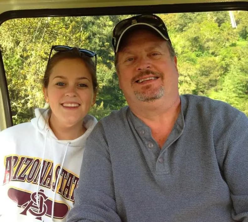 Rudy and one of his daughters smile together in a golf cart.