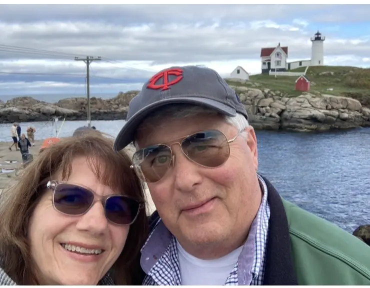 Nancy and Steve taking a selfie by the water with a lighthouse behind them.