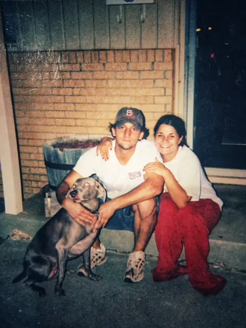 Josh hugs his gray dog while sitting on a front step with Beth.