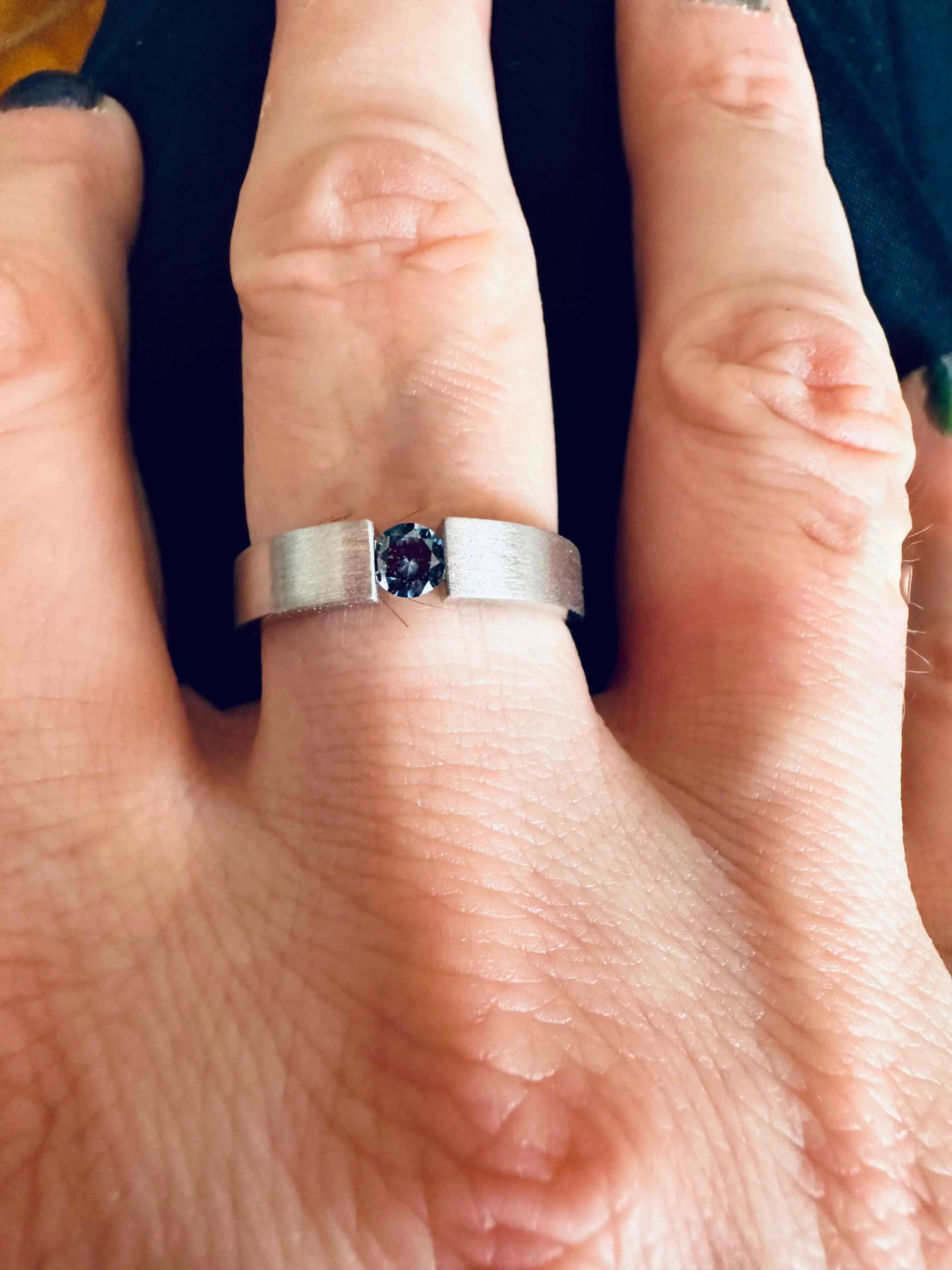 Hand wearing a brushed silver band set with a single blue stone.