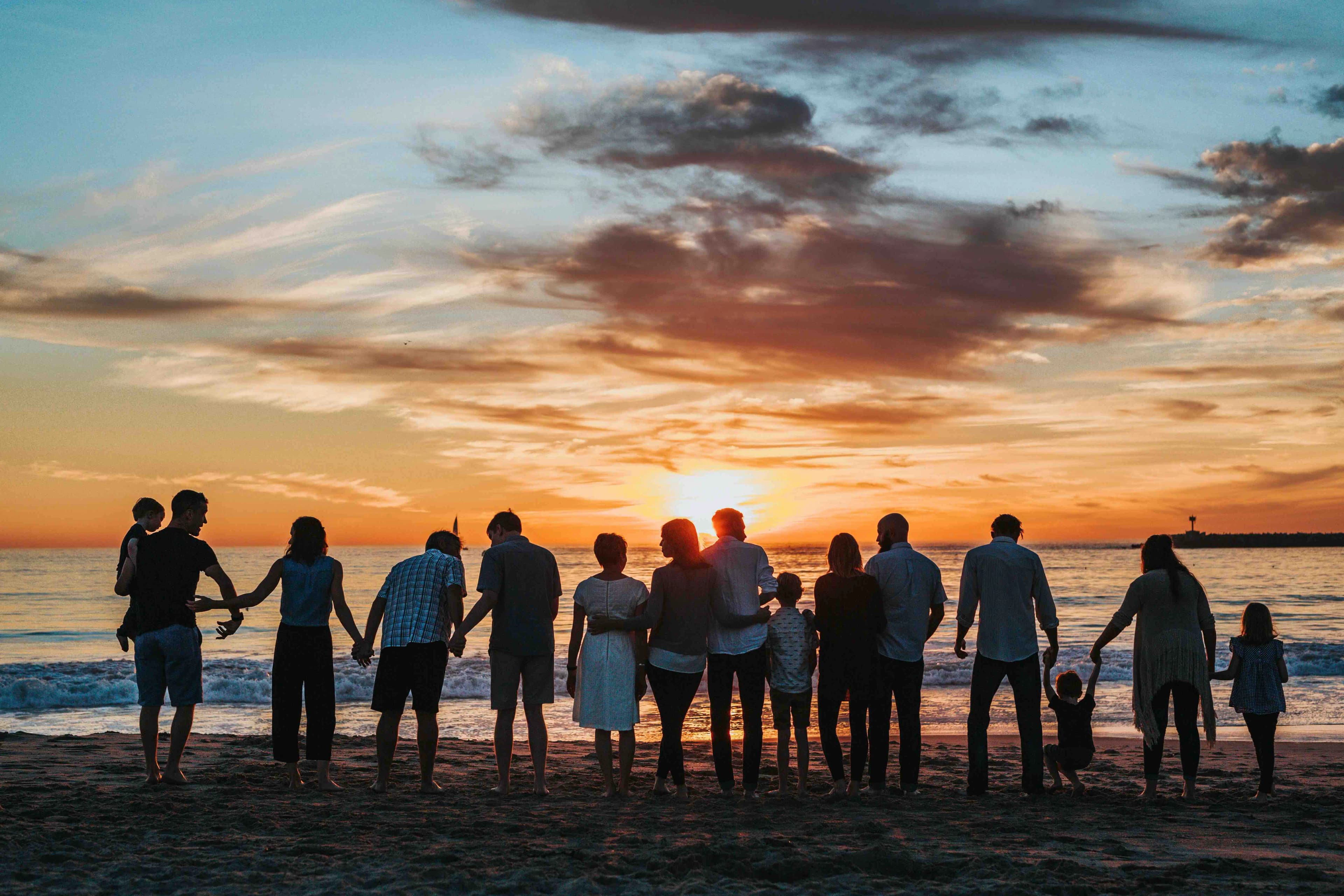 families link hands and face the ocean during sunset