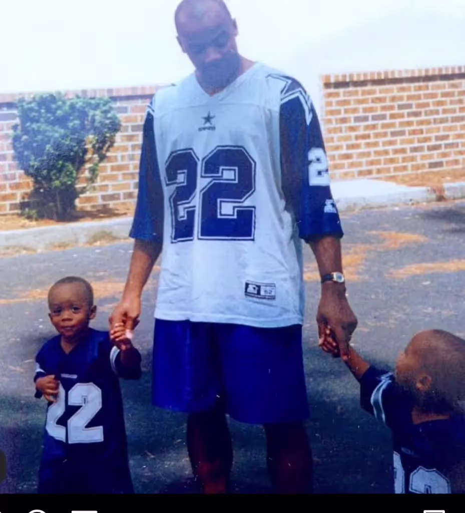Father in a Cowboys No. 22 jersey holding hands with two young sons in matching jerseys.