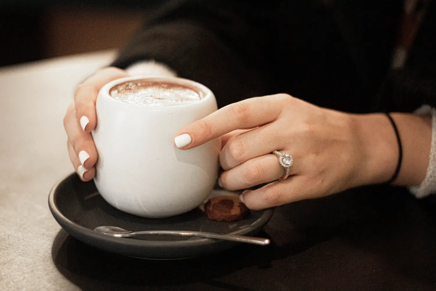 Woman holding a cup of coffee while wearing a diamond ring.
