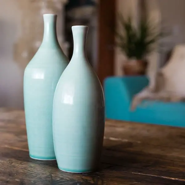 Two pale aqua ceramic bottle vases on a wooden table.
