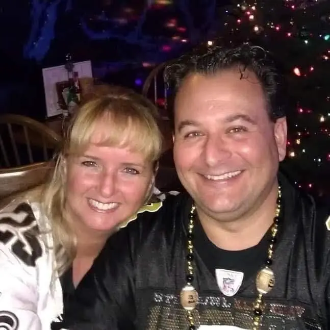 Daisy and Jay smiling cheek to cheek in front of a lit Christmas tree.