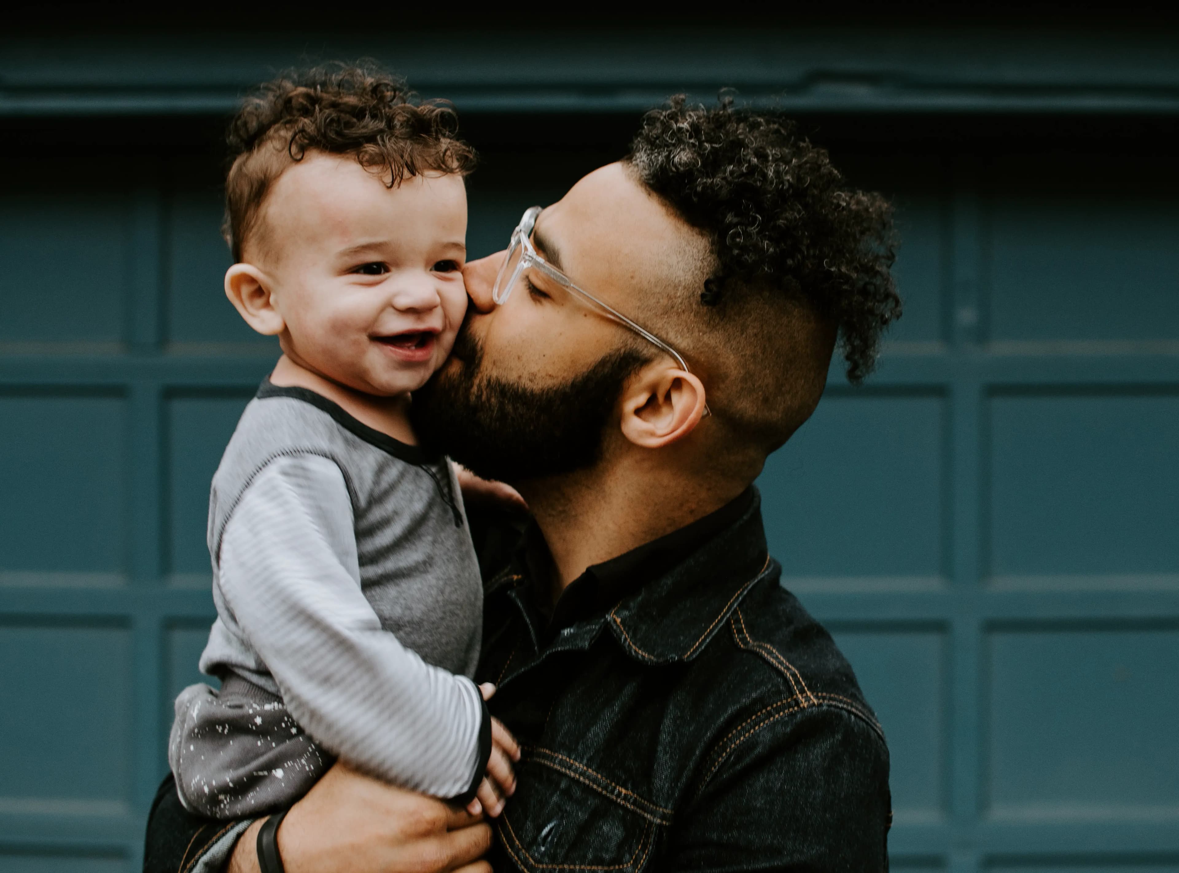 A smiling toddler gets a kiss on the cheek from his father.