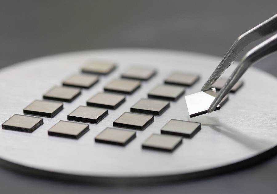 Square CVD diamond plates on a metal surface in a laboratory, with tweezers lifting one diamond seed.