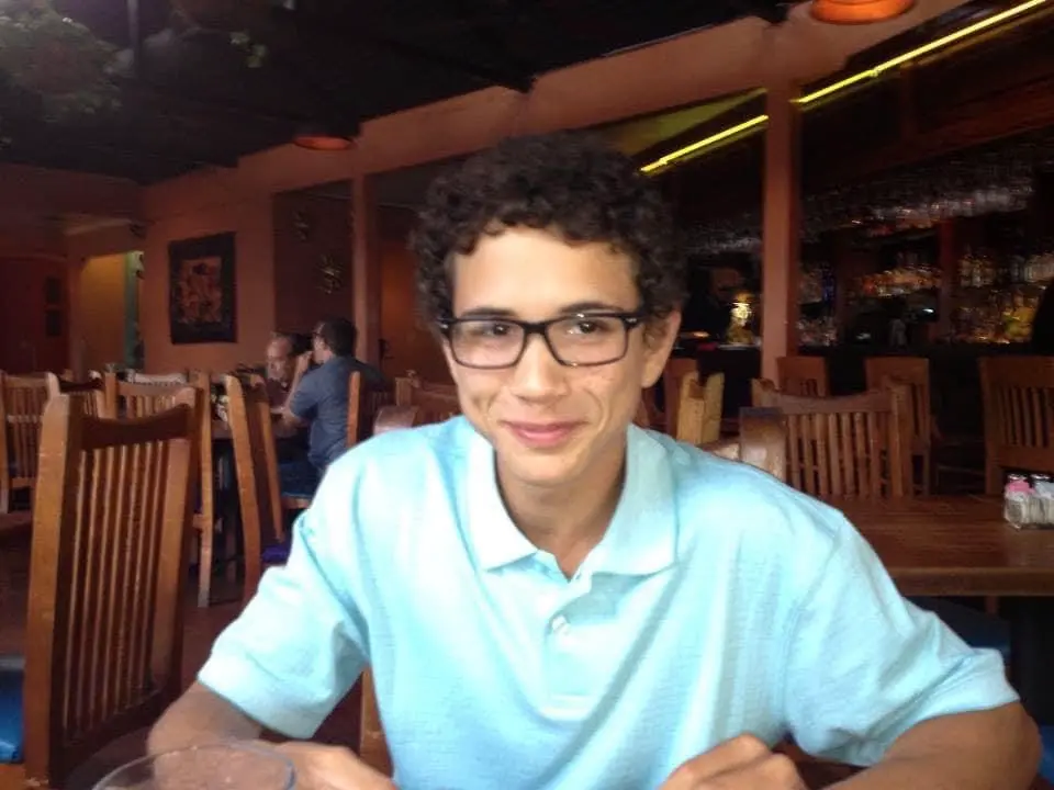 Smiling young man in glasses and a light blue polo at a restaurant table.