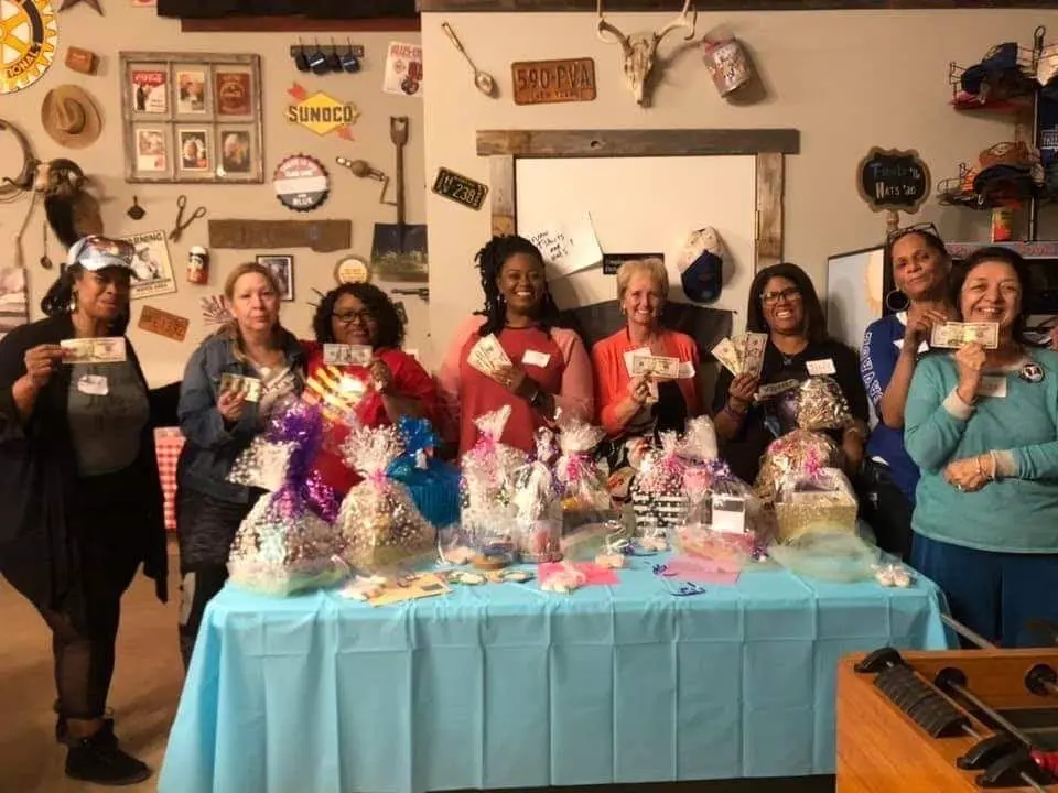 Group of smiling women holding gifts behind a table lined with wrapped gift bags.