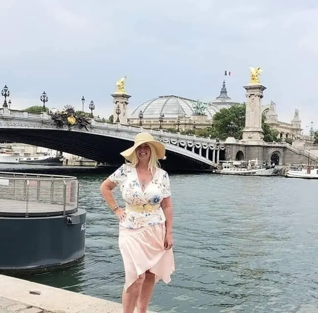Daisy in a sun hat and floral top posing by the Seine in Paris.