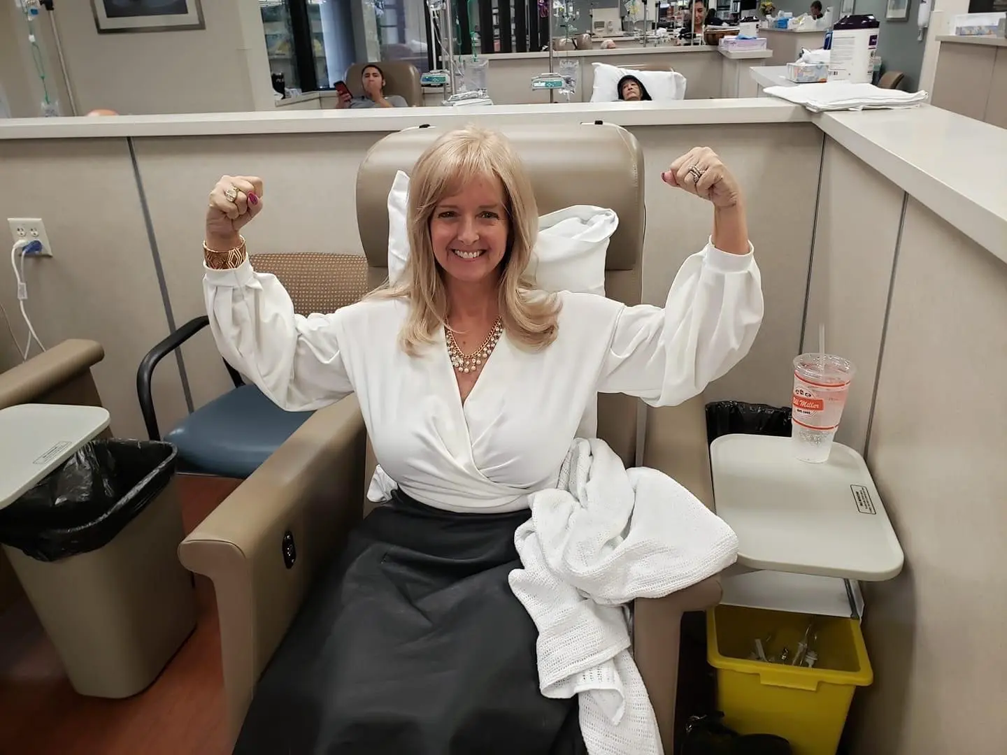 Daisy flexing both arms with a big smile in a treatment chair.