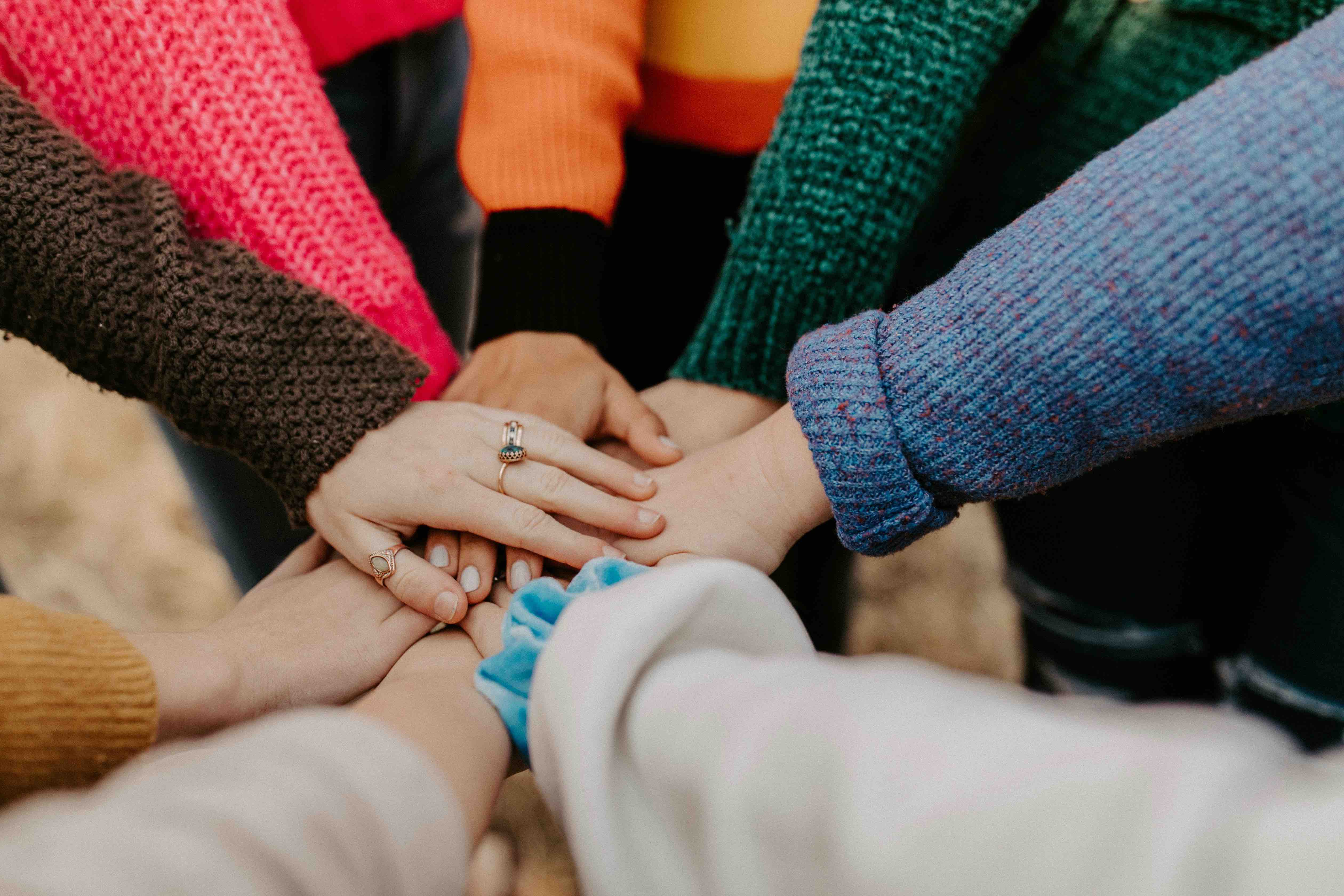 A group of people in colorful sweaters stacking their hands together in the center