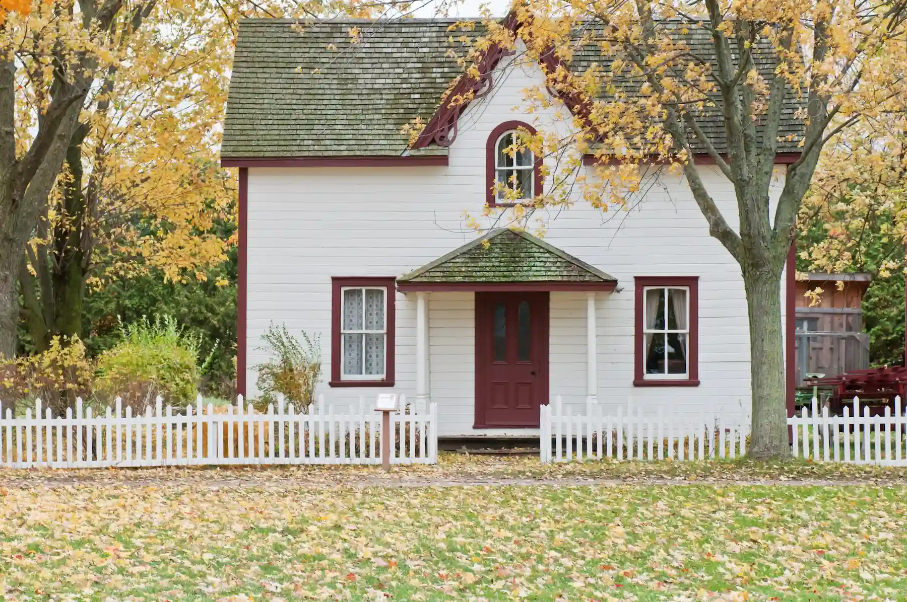 Leaves covering the front yard of a white house during fall.