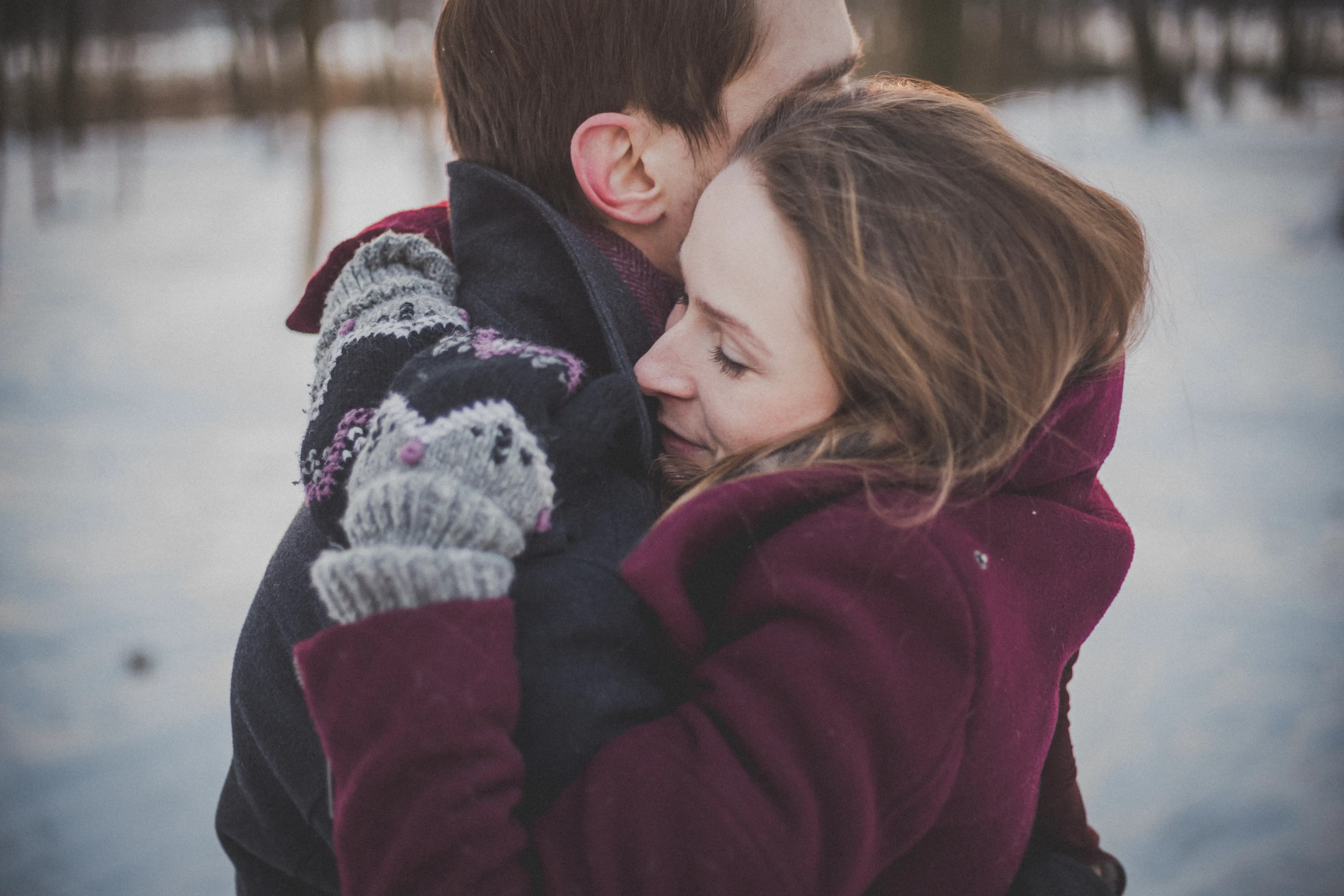 A couple in winter coats and mittens embracing in the snow