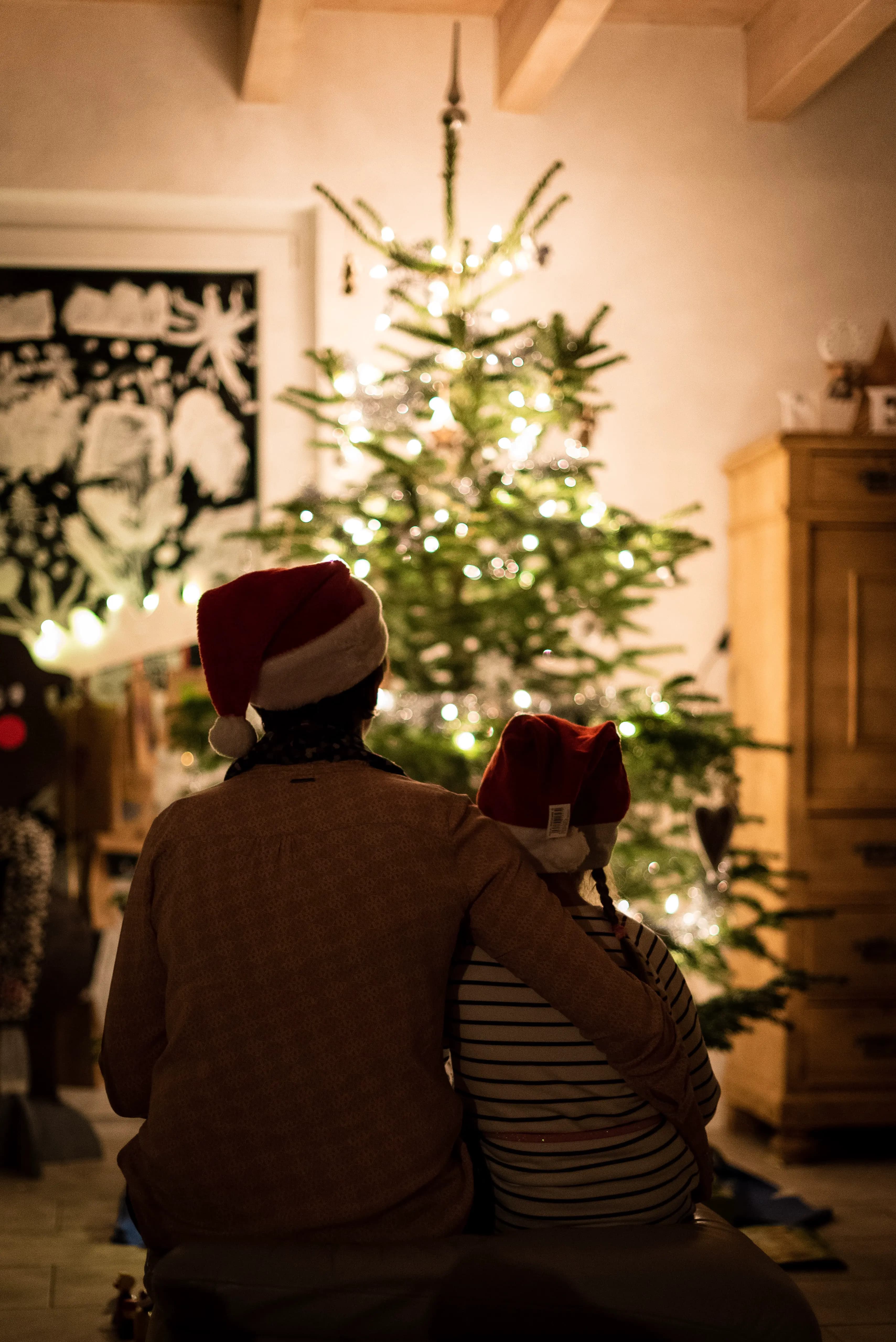 Two people in Santa hats sitting together in front of a lit Christmas tree