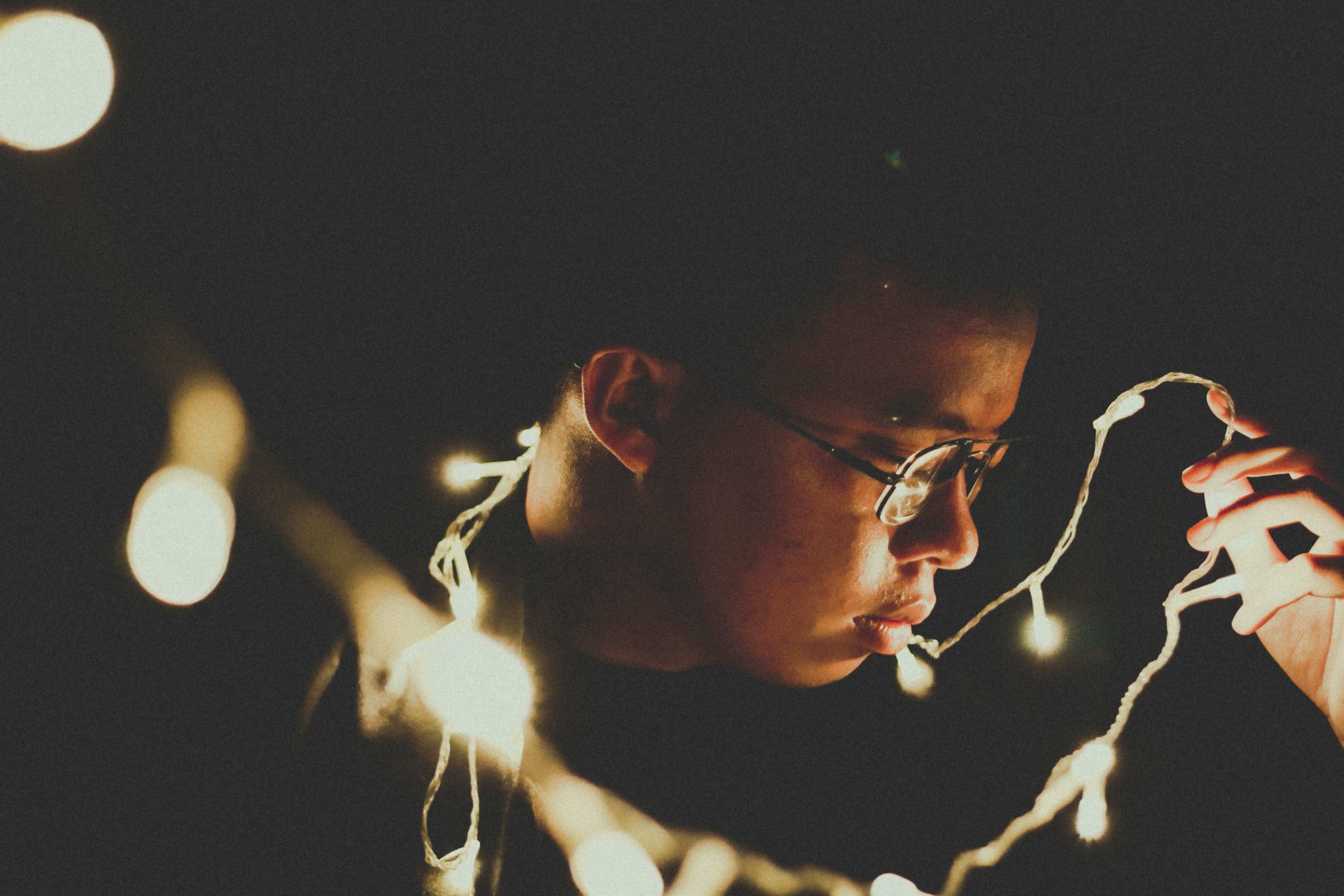A young man in glasses holding a strand of glowing string lights in the dark