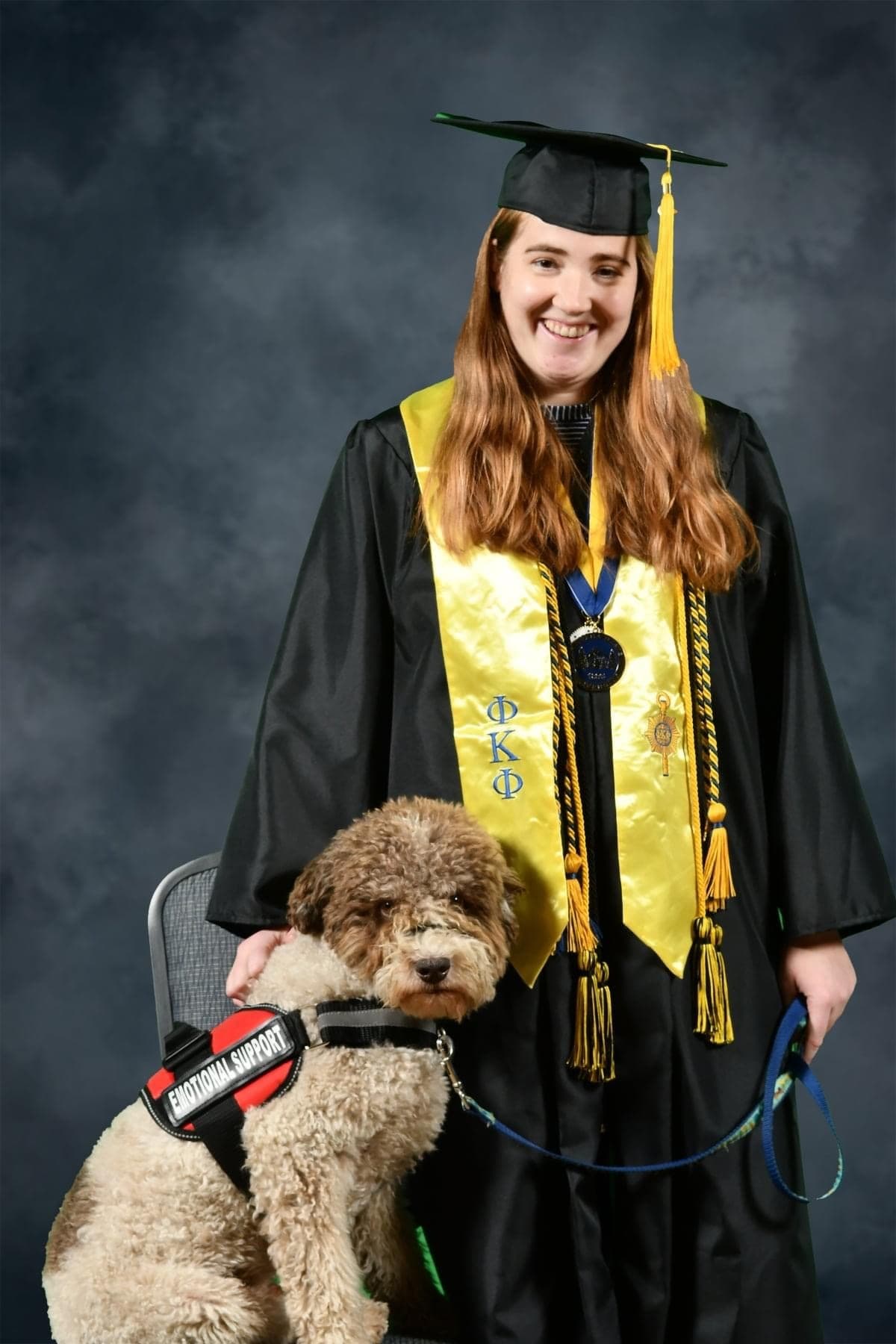 Emilie in her graduation cap and gown poses with Orio, who wears a service vest.