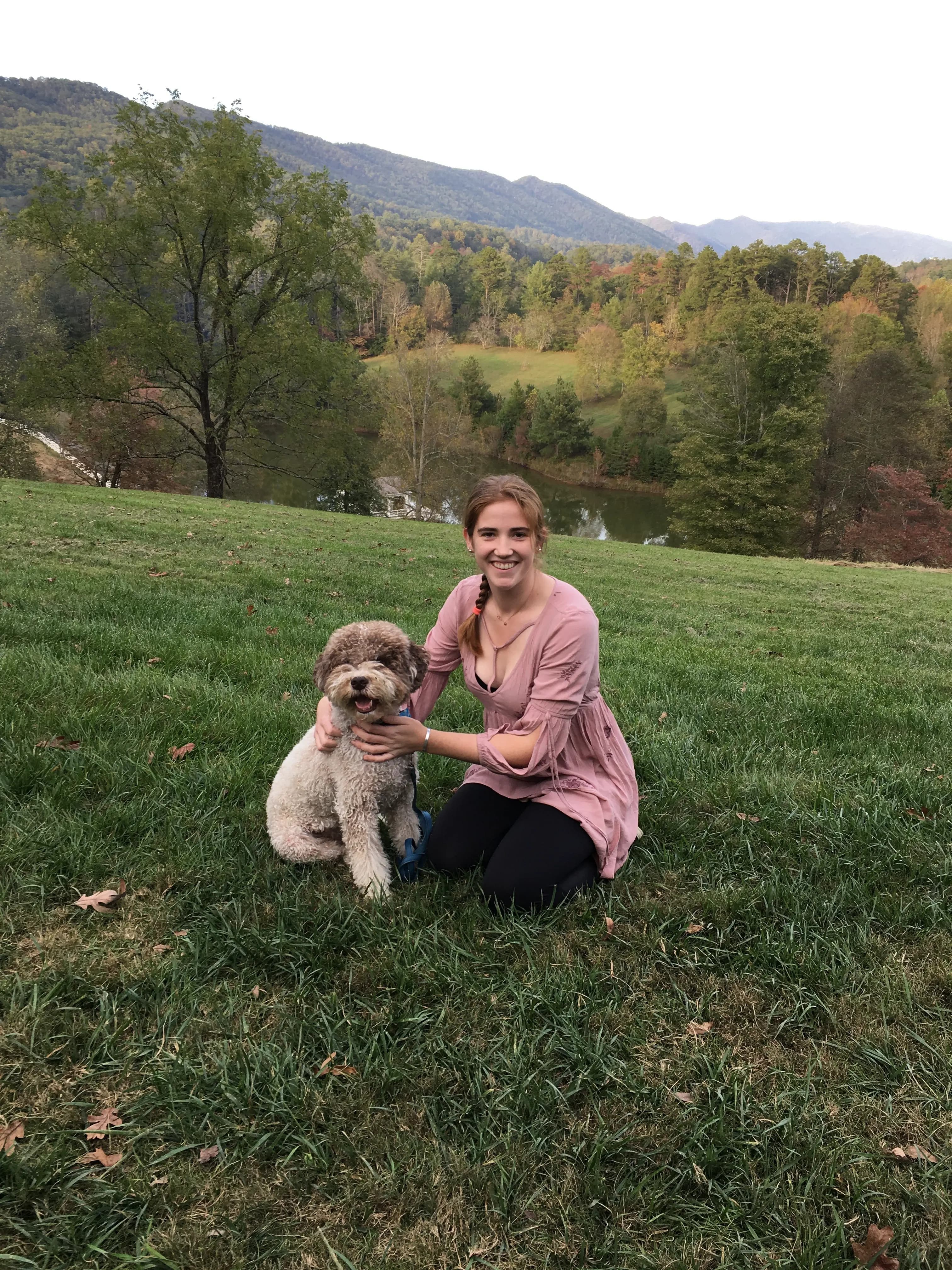 Emilie kneels in a grassy meadow beside Orio with mountains behind them.