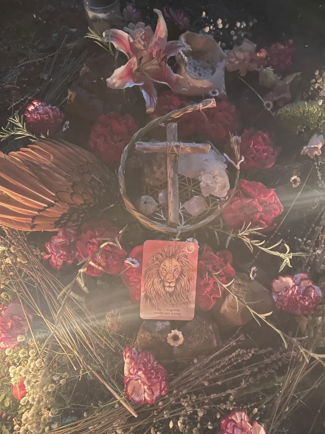 Lilies, roses, and dried grasses gathered around a small cross and a lion card, from Lyon’s ceremony