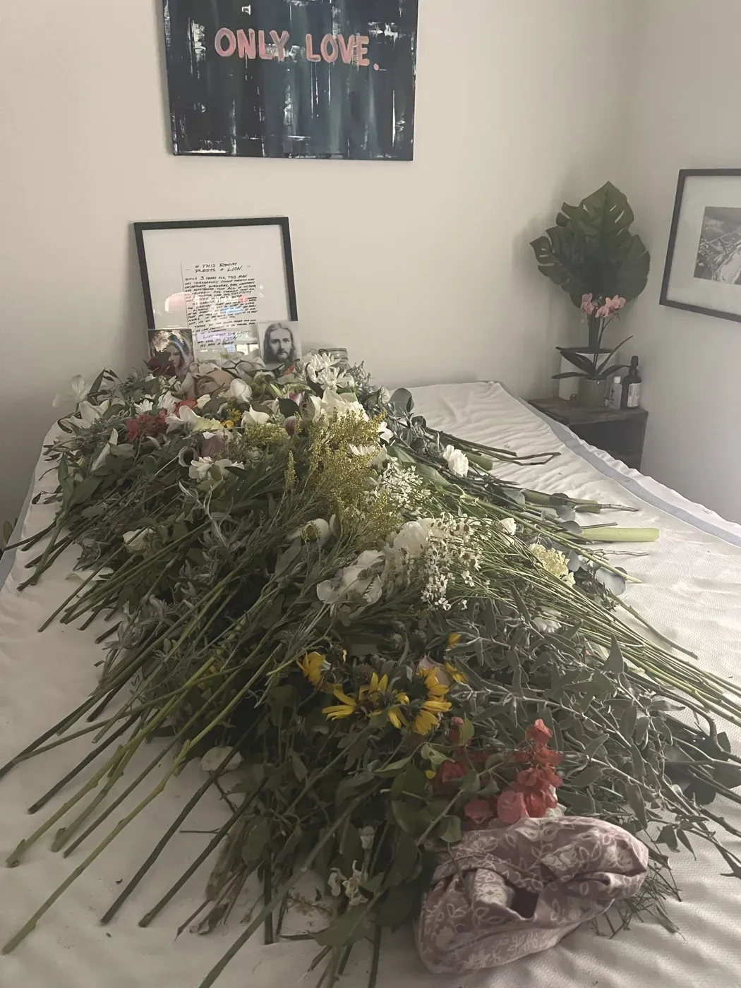 Armfuls of fresh flowers laid across a white bed in a sunlit room, from Lyon’s living memorial