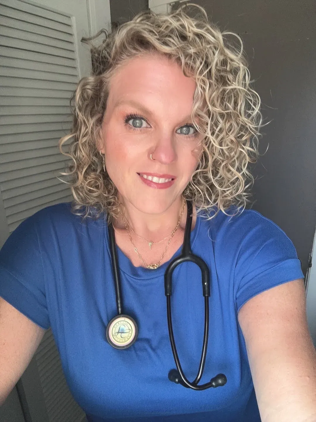 Kacie Gikonyo smiling in her blue nursing scrubs, a stethoscope around her neck, in a polaroid print